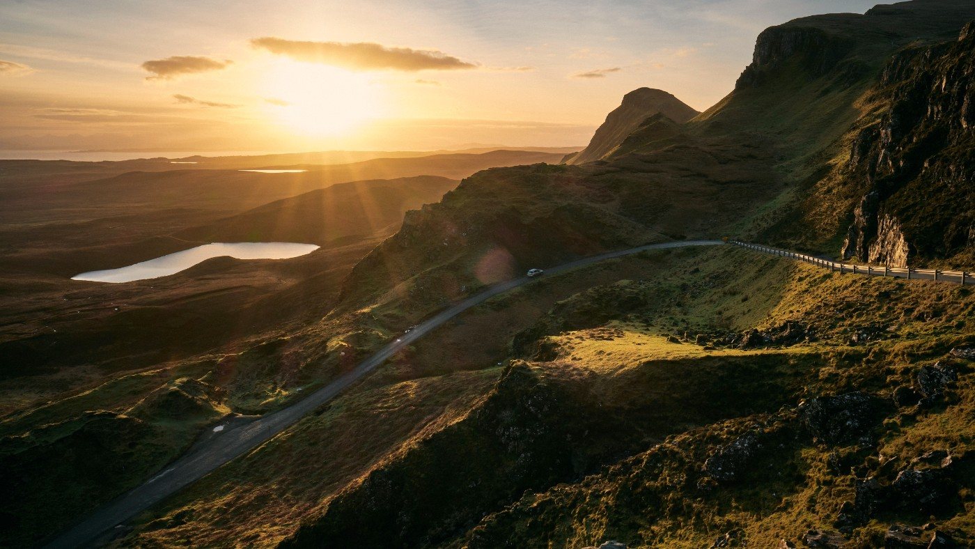 The single-track road over the Quiraing on Skye, curving along the ridge as a low sun breaks over the sea