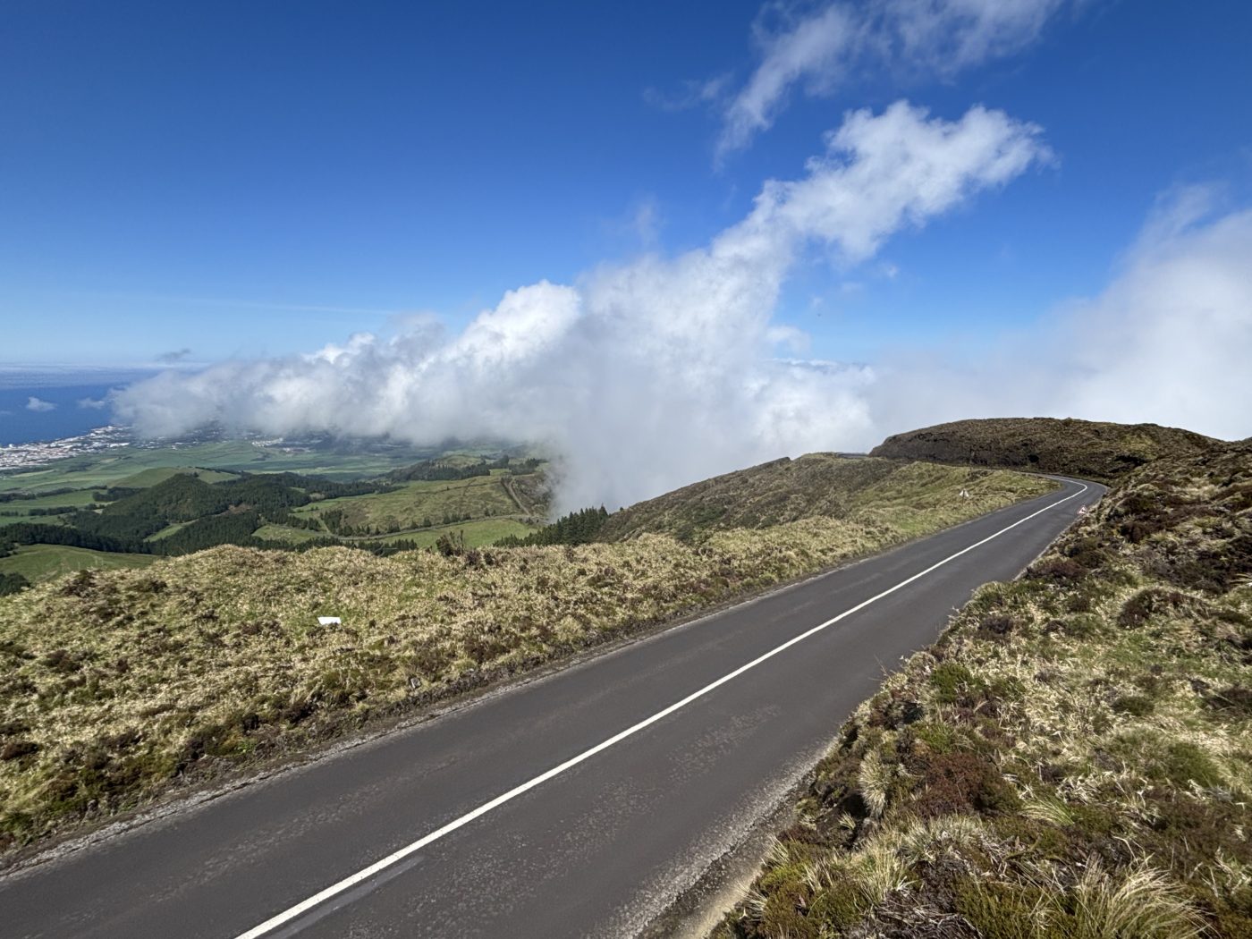 A mountain road sweeping toward a bank of cloud rolling over the ridge in the Azores