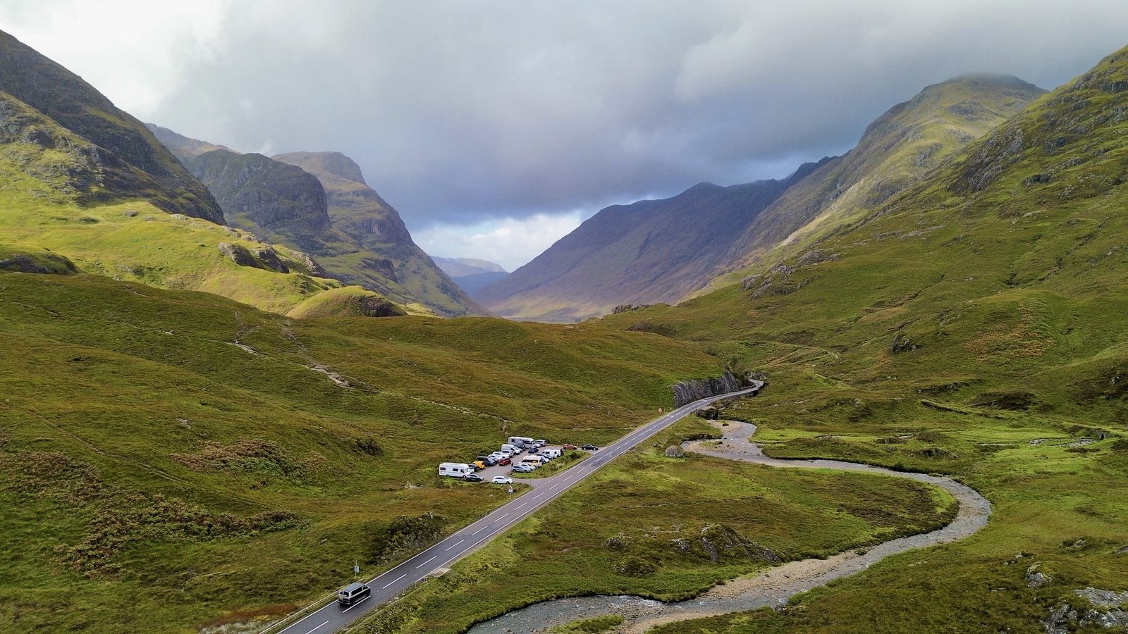 The A82 running through Glencoe between the Three Sisters, a van on the road and the river winding alongside
